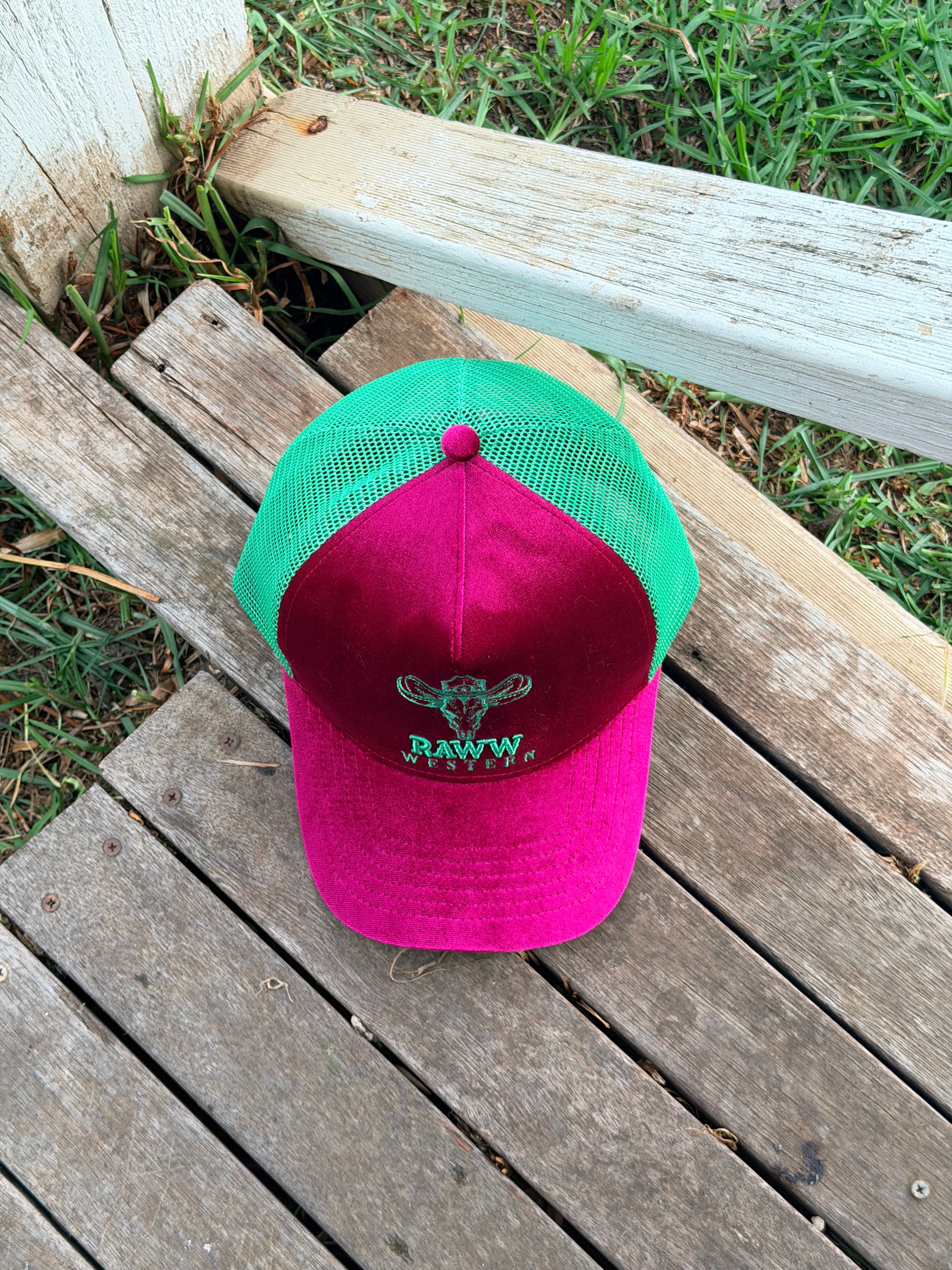Ruby velvet trucker cap with green mesh back and RAW WES tern logo, on wooden boards