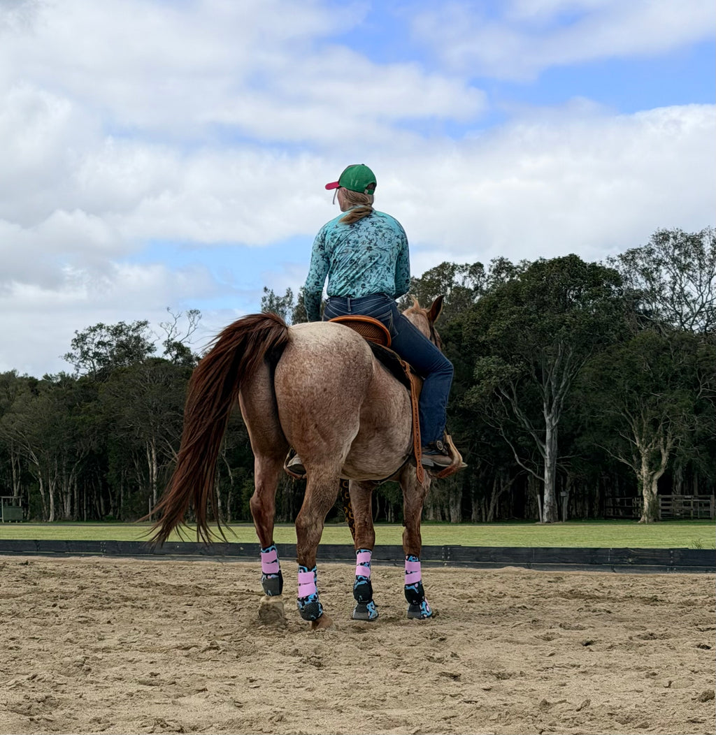 Leopard-print splint boots on horse from behind, pink cuffs and blue patterned uppers