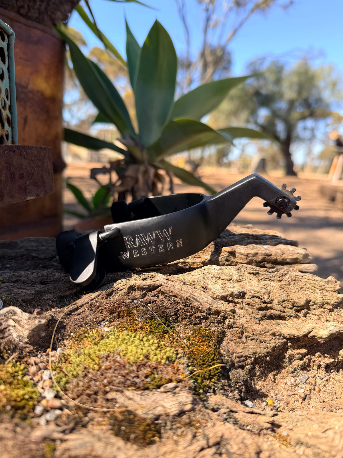 Black Western spurs on a rock with RAW WESTERN branding on strap