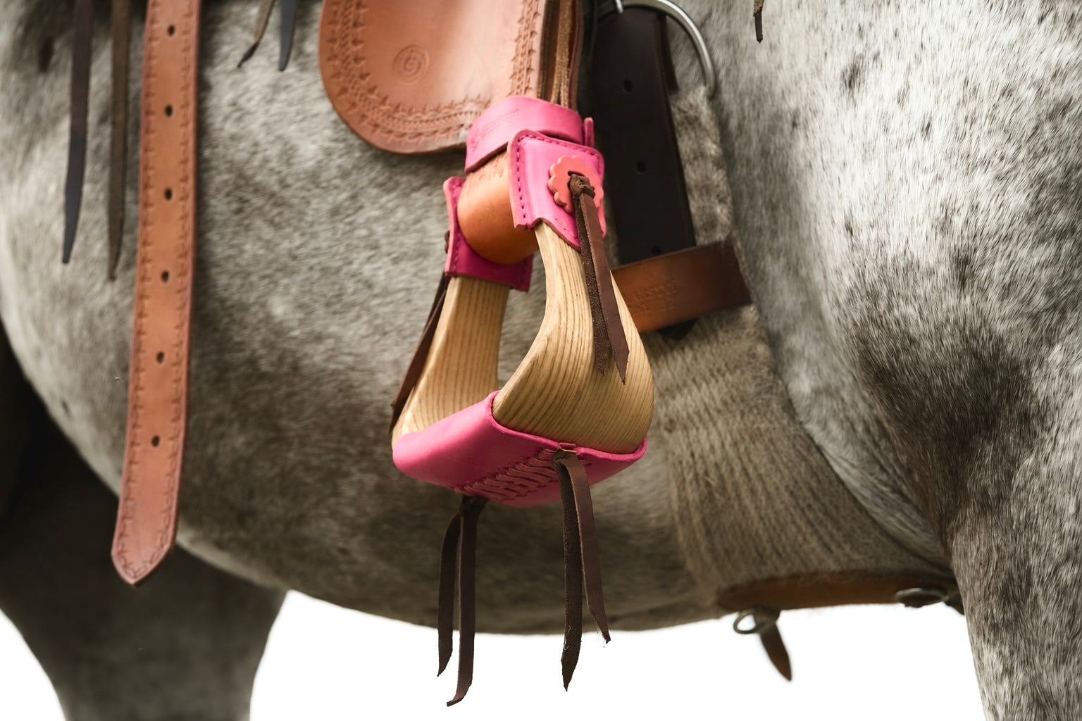 Pink western stirrups with leather straps and metal buckles on a saddle