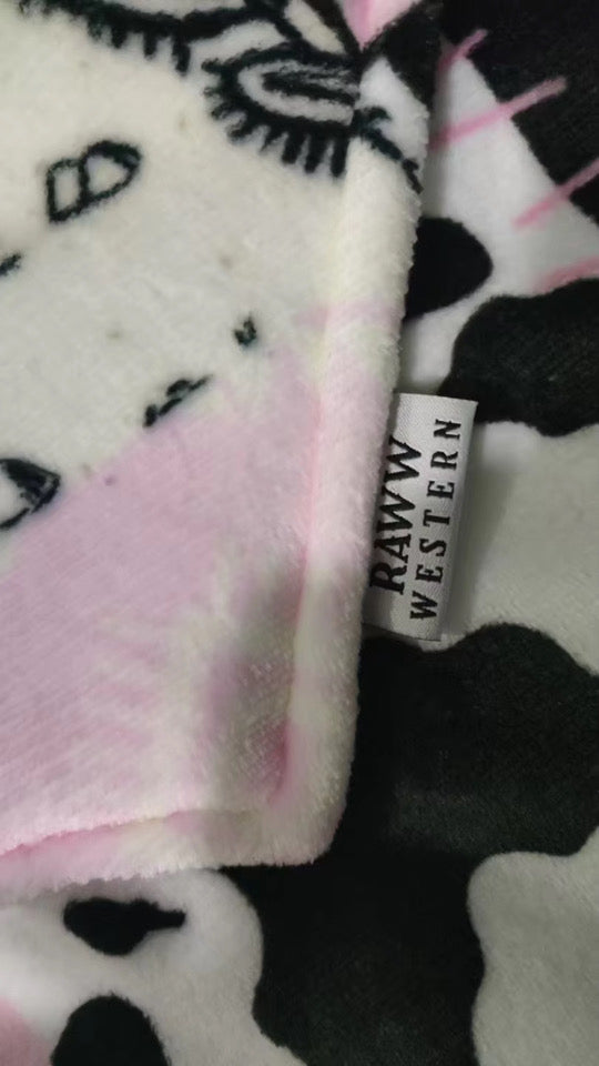 Fleece hoodie blanket fabric close-up with pink tint, black cow and cactus prints